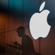 A silhouette of a man using an iPhone in front of the Apple logo.